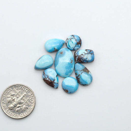 Golden Hills Turquoise cabochons, icy blue to lavender tones with chocolate matrix, polished stones on a white background with a US dime for scale