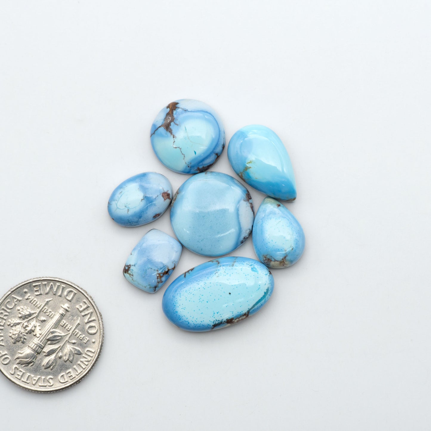 Golden Hills Turquoise cabochons, icy blue to lavender tones with chocolate matrix, polished stones on a white background with a US dime for scale
