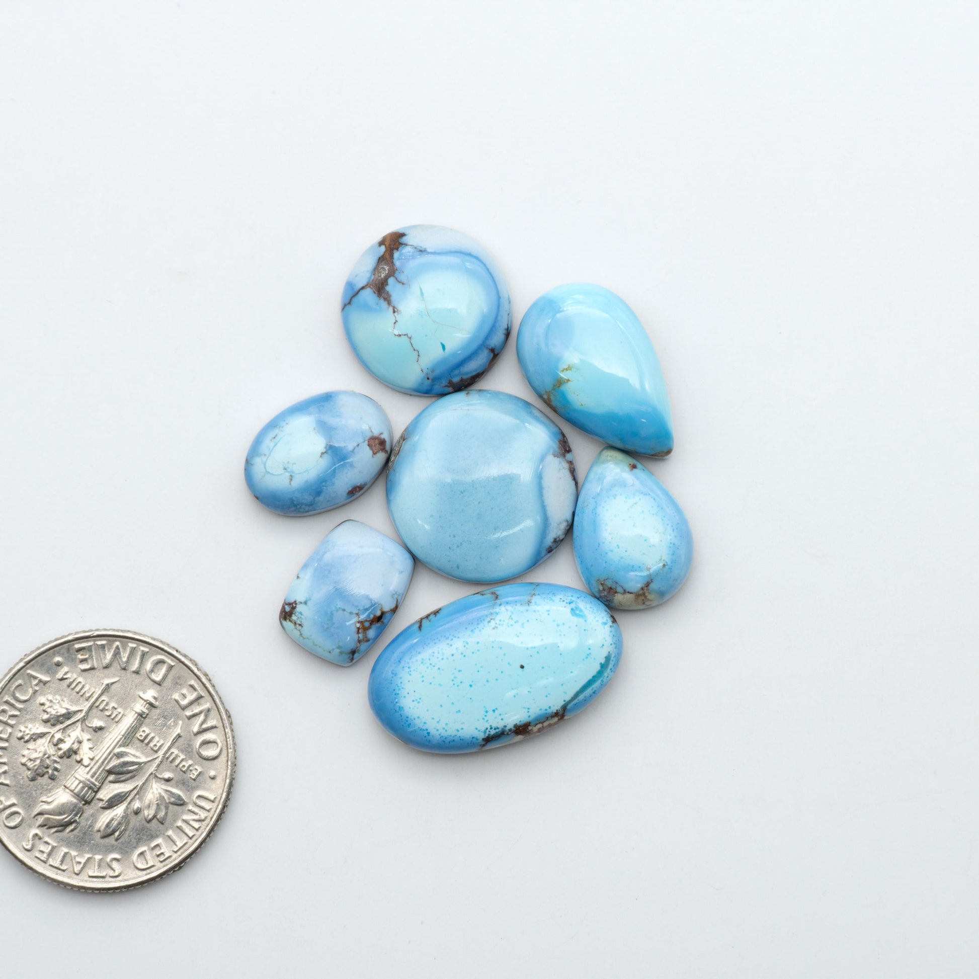 Golden Hills Turquoise cabochons, icy blue to lavender tones with chocolate matrix, polished stones on a white background with a US dime for scale