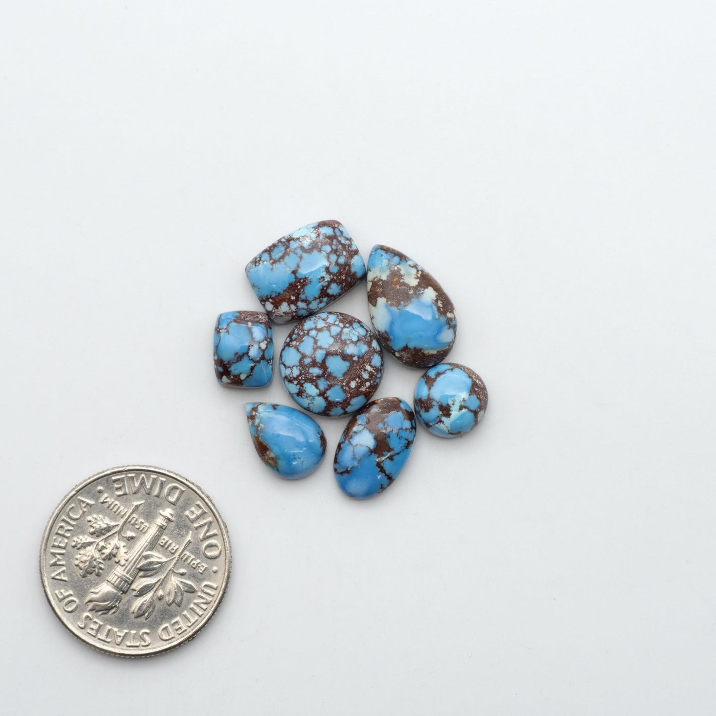 Golden Hills Turquoise cabochons, icy blue to lavender tones with chocolate matrix, polished stones on a white background with a US dime for scale