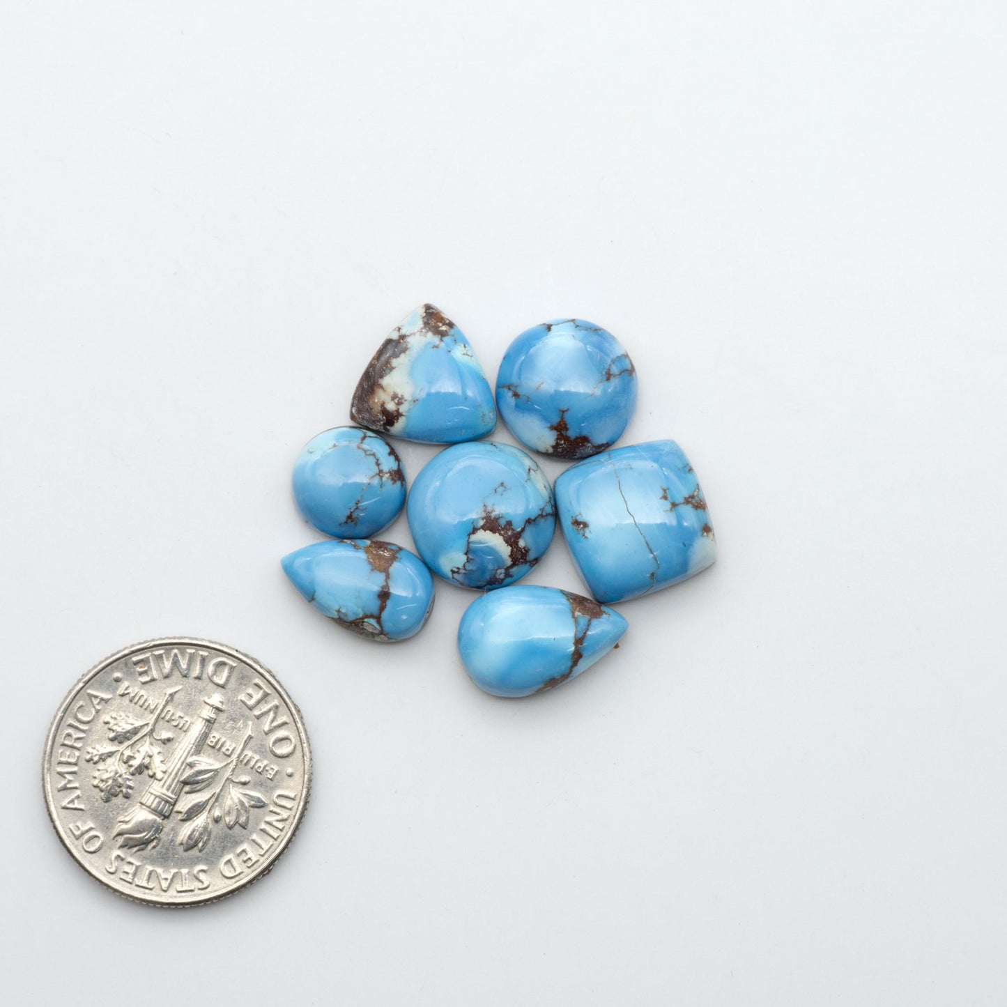 Golden Hills Turquoise cabochons, icy blue to lavender tones with chocolate matrix, polished stones on a white background with a US dime for scale