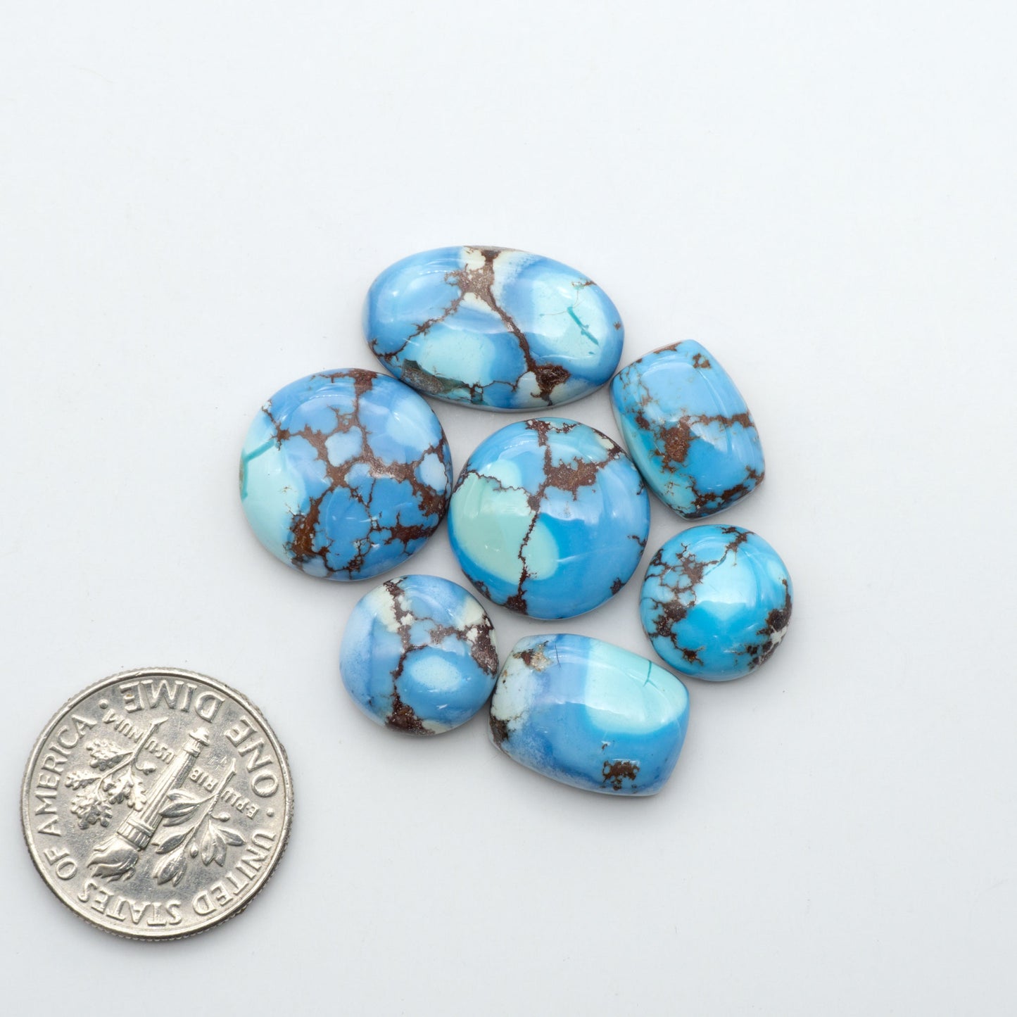 Golden Hills Turquoise cabochons, icy blue to lavender tones with chocolate matrix, polished stones on a white background with a US dime for scale