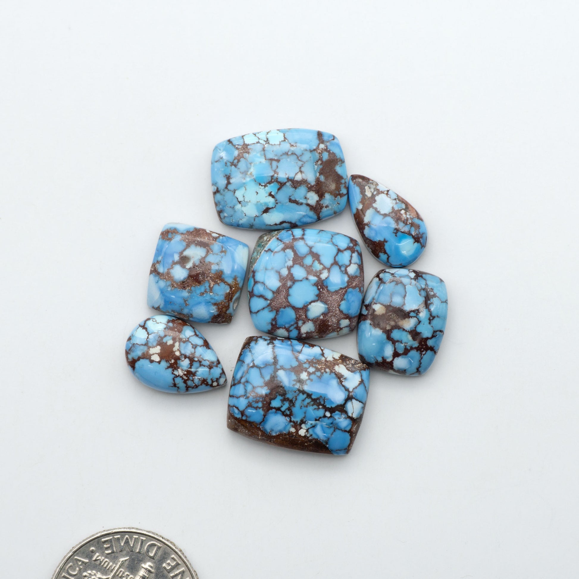 Golden Hills Turquoise cabochons, icy blue to lavender tones with chocolate matrix, polished stones on a white background with a US dime for scale