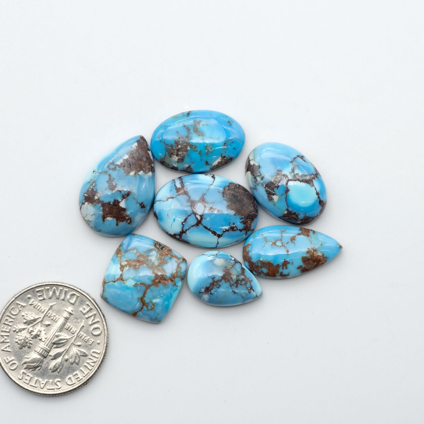 Golden Hills Turquoise cabochons, icy blue to lavender tones with chocolate matrix, polished stones on a white background with a US dime for scale