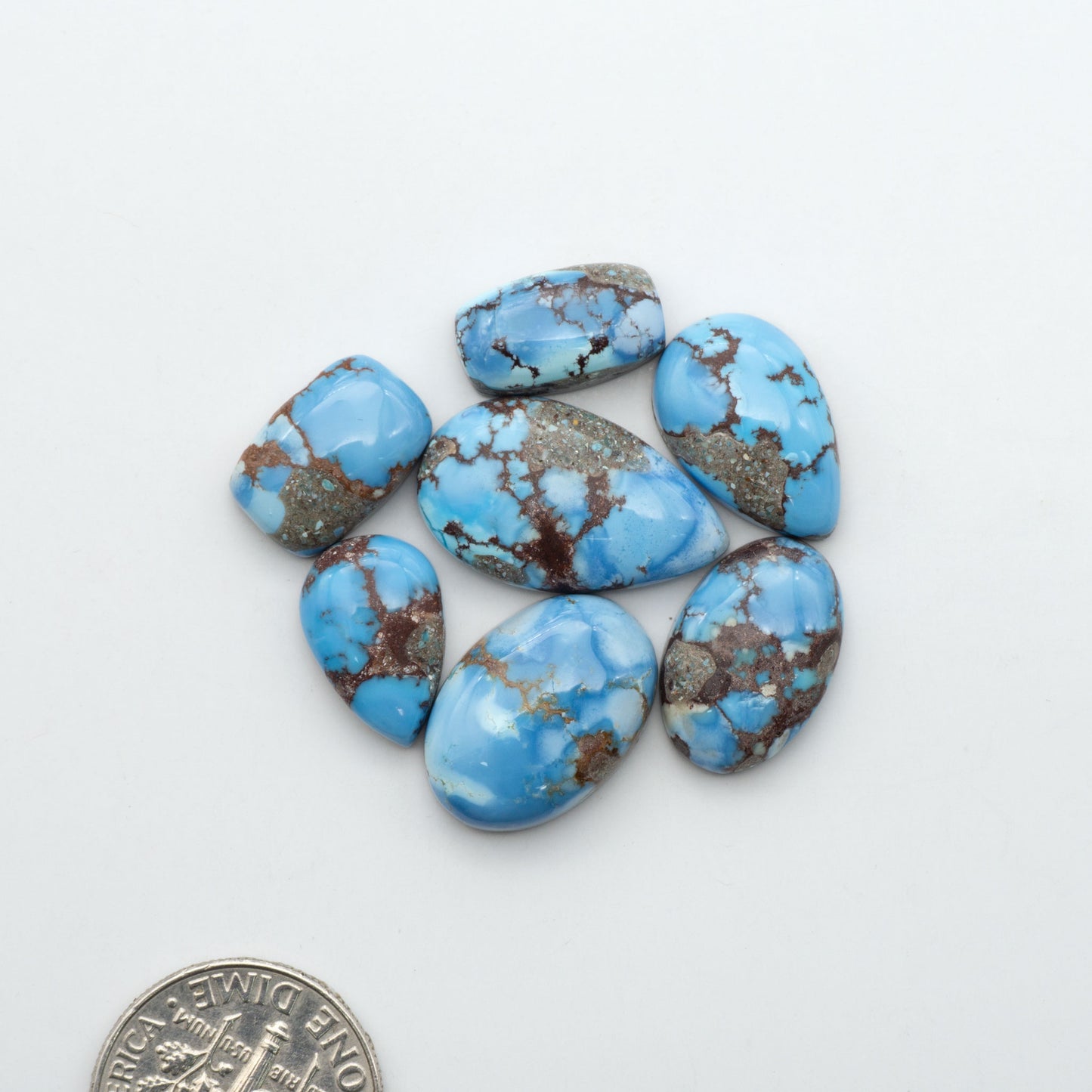 Golden Hills Turquoise cabochons, icy blue to lavender tones with chocolate matrix, polished stones on a white background with a US dime for scale