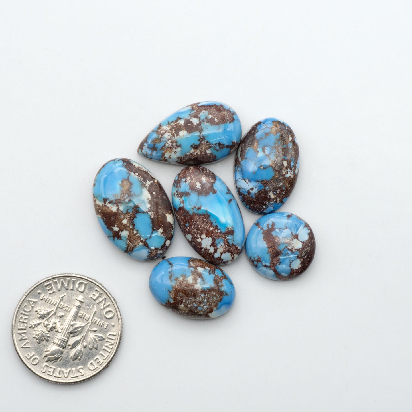 Golden Hills Turquoise cabochons, icy blue to lavender tones with chocolate matrix, polished stones on a white background with a US dime for scale