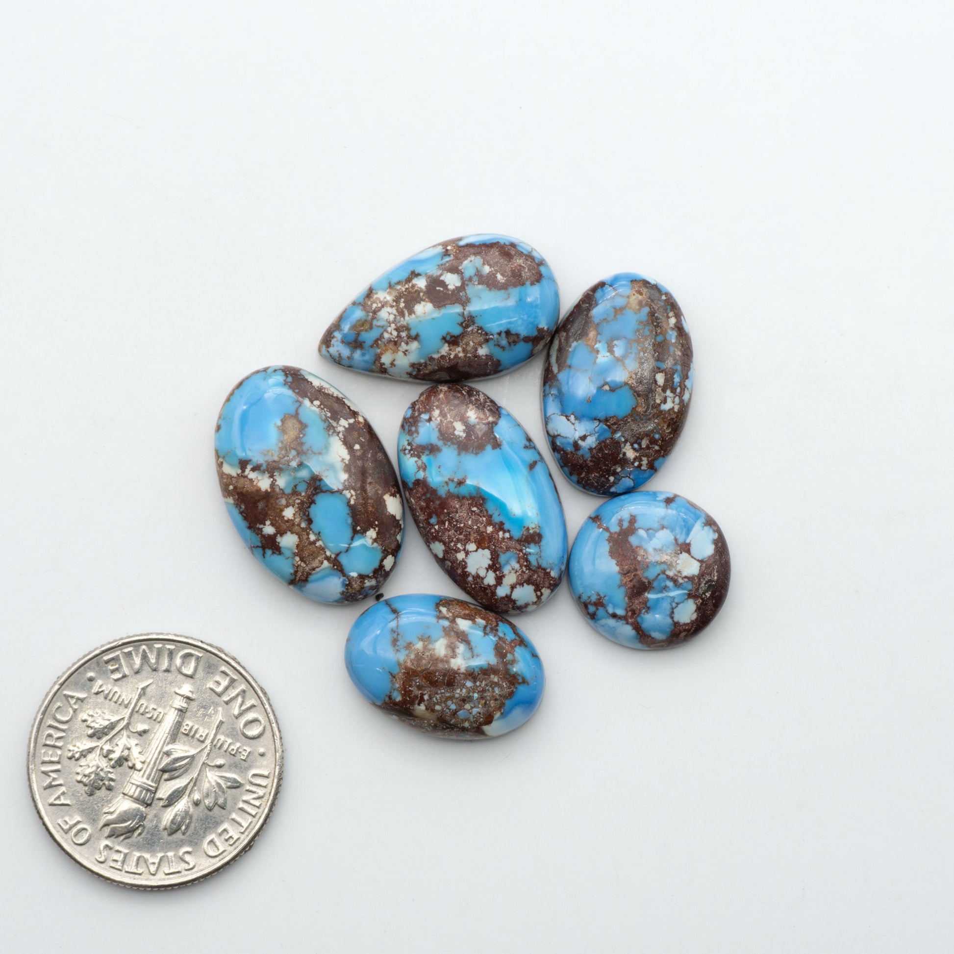 Golden Hills Turquoise cabochons, icy blue to lavender tones with chocolate matrix, polished stones on a white background with a US dime for scale