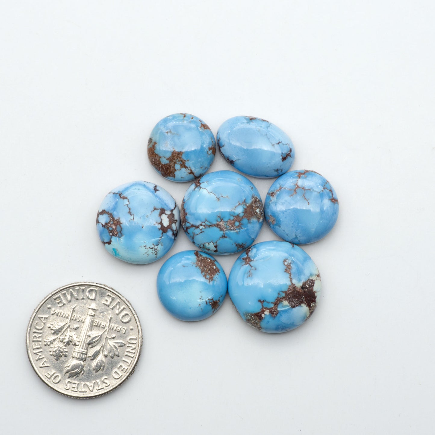 Golden Hills Turquoise cabochons, icy blue to lavender tones with chocolate matrix, polished stones on a white background with a US dime for scale