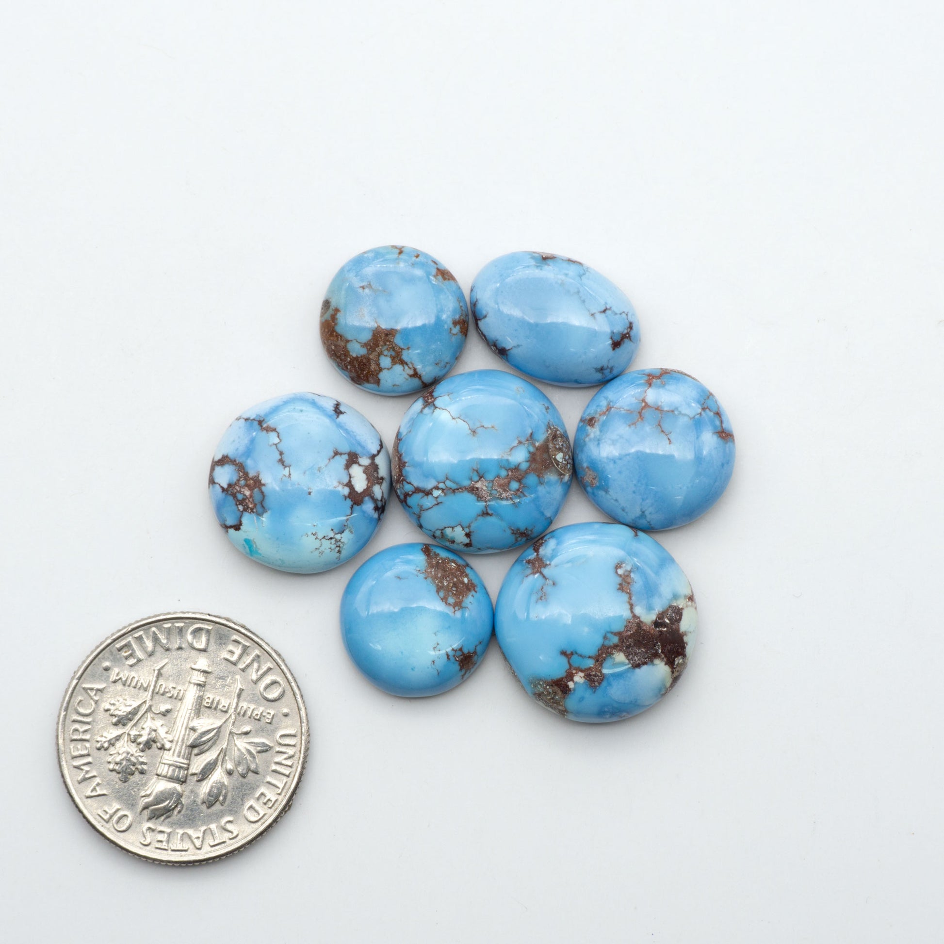 Golden Hills Turquoise cabochons, icy blue to lavender tones with chocolate matrix, polished stones on a white background with a US dime for scale