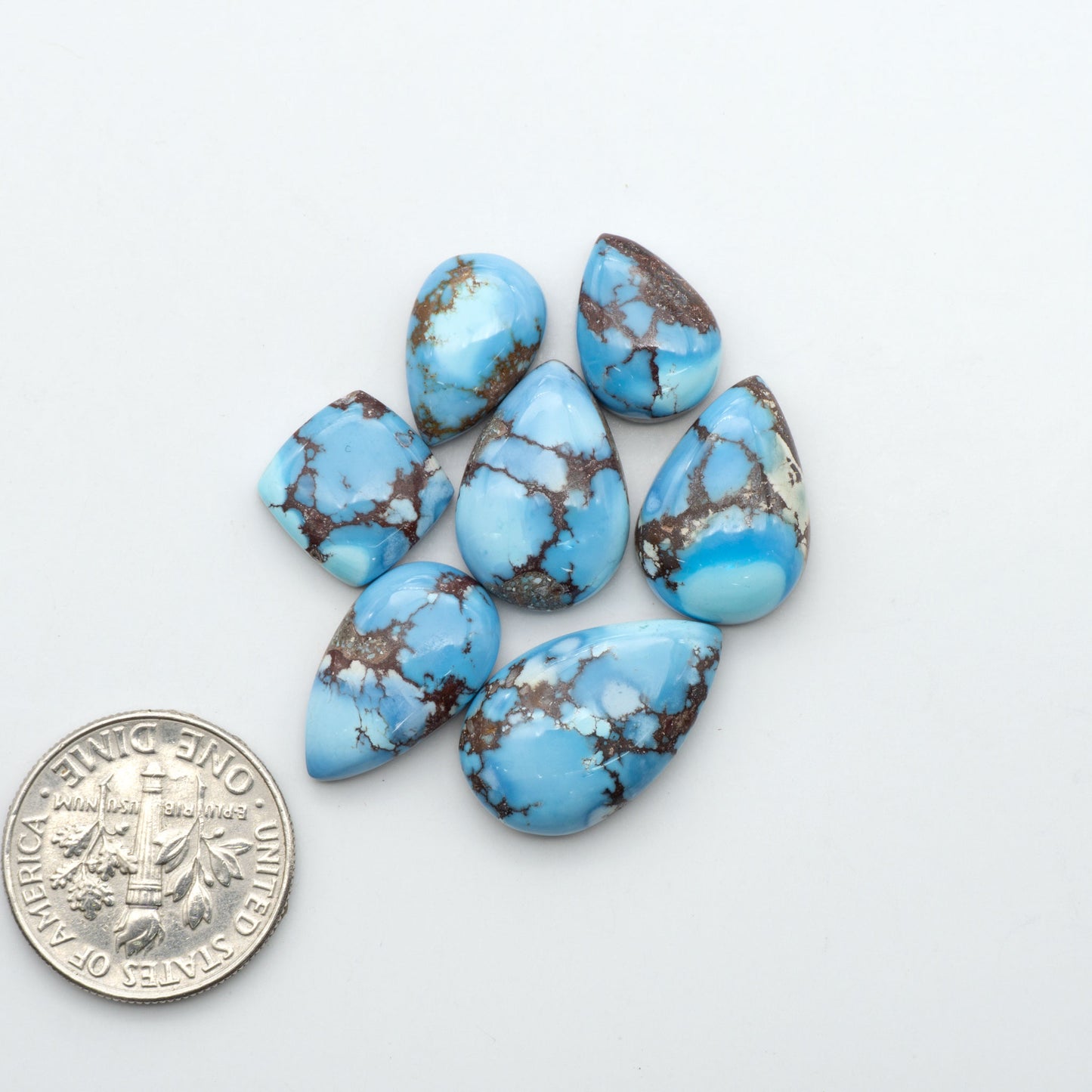 Golden Hills Turquoise cabochons, icy blue to lavender tones with chocolate matrix, polished stones on a white background with a US dime for scale