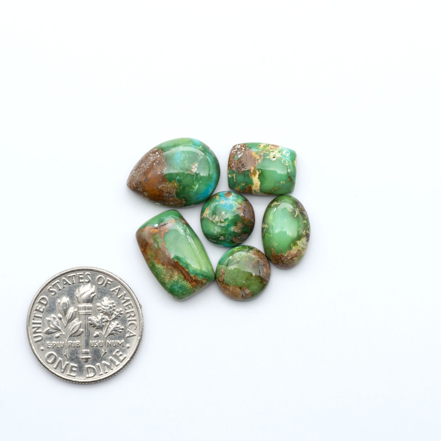 Sonoran Mountain Turquoise cabochons, blue-green color with natural matrix, polished stones on a white background, with a US dime for scale