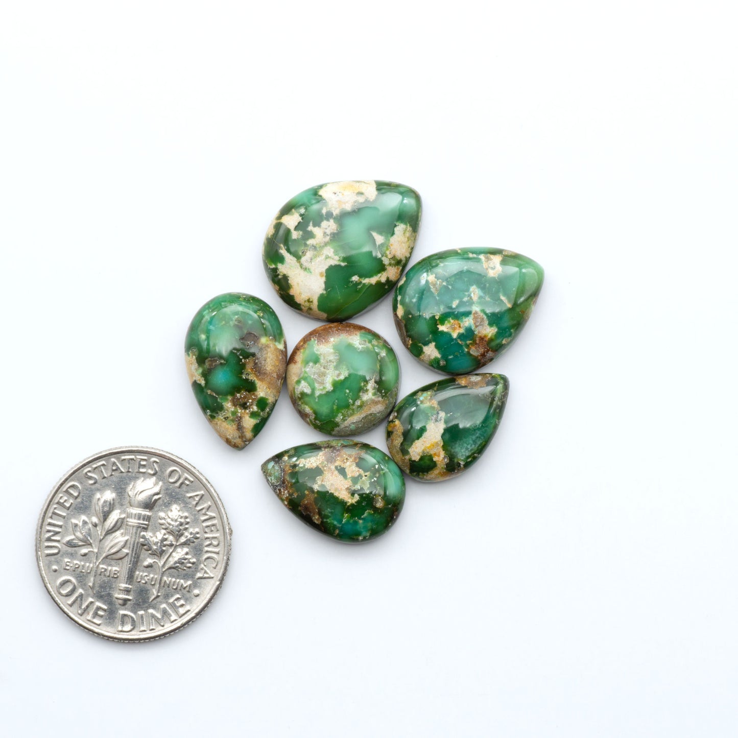 Sonoran Mountain Turquoise cabochons, blue-green color with natural matrix, polished stones on a white background, with a US dime for scale