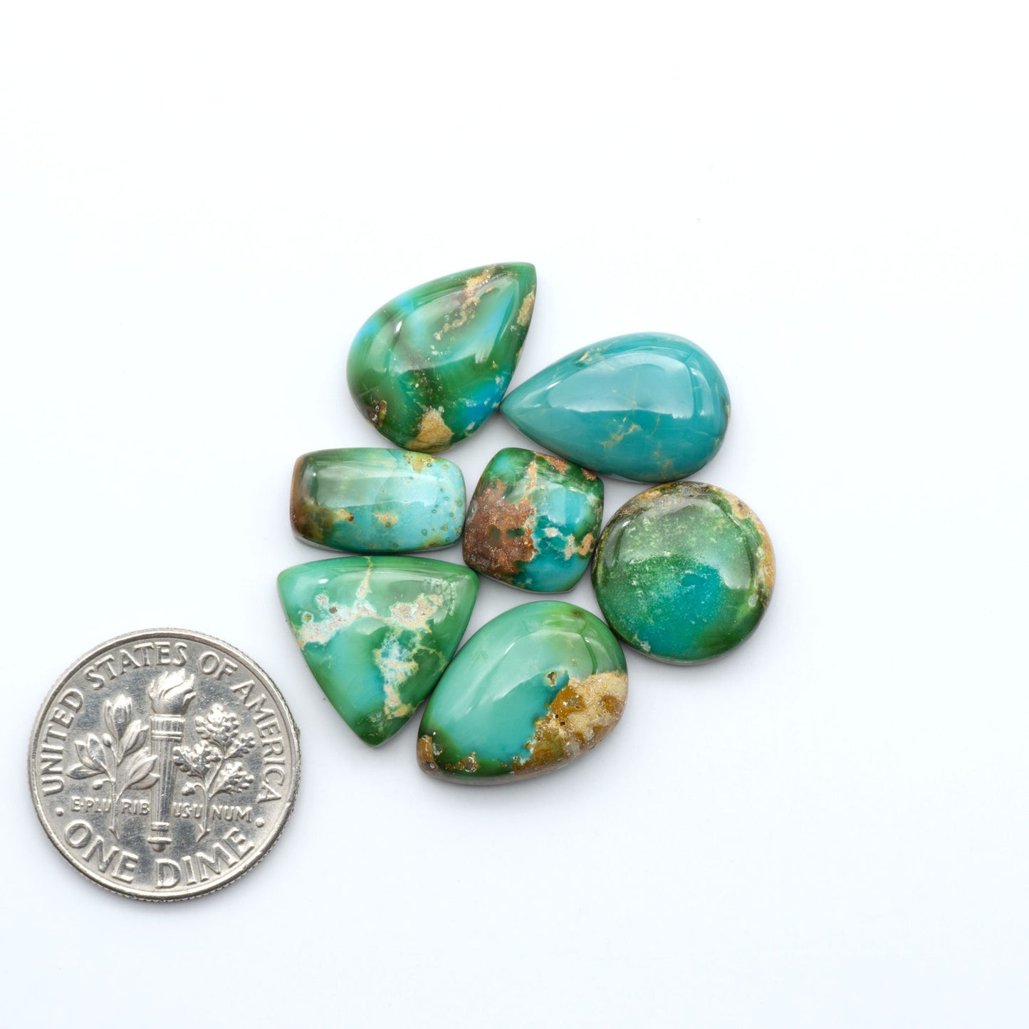 Sonoran Mountain Turquoise cabochons, blue-green color with natural matrix, polished stones on a white background, with a US dime for scale