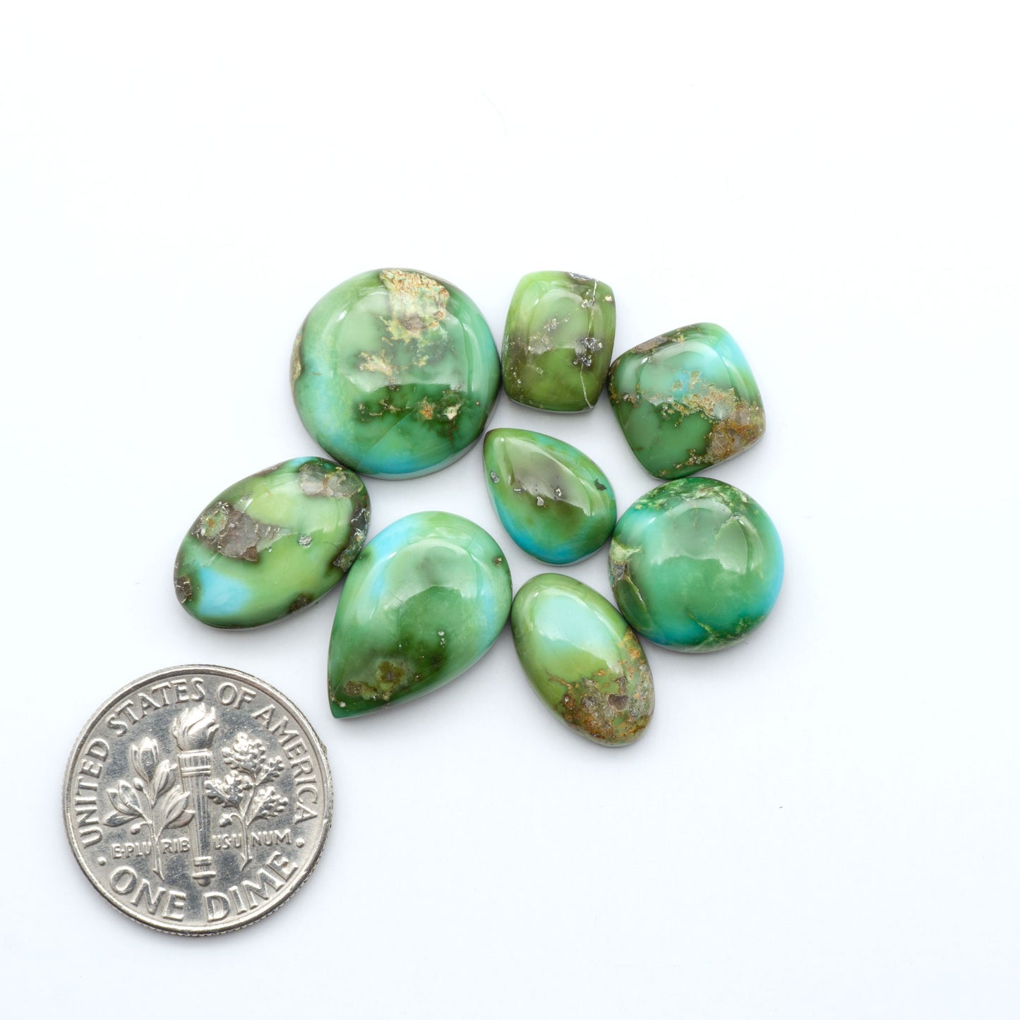 Sonoran Mountain Turquoise cabochons, blue-green color with natural matrix, polished stones on a white background, with a US dime for scale