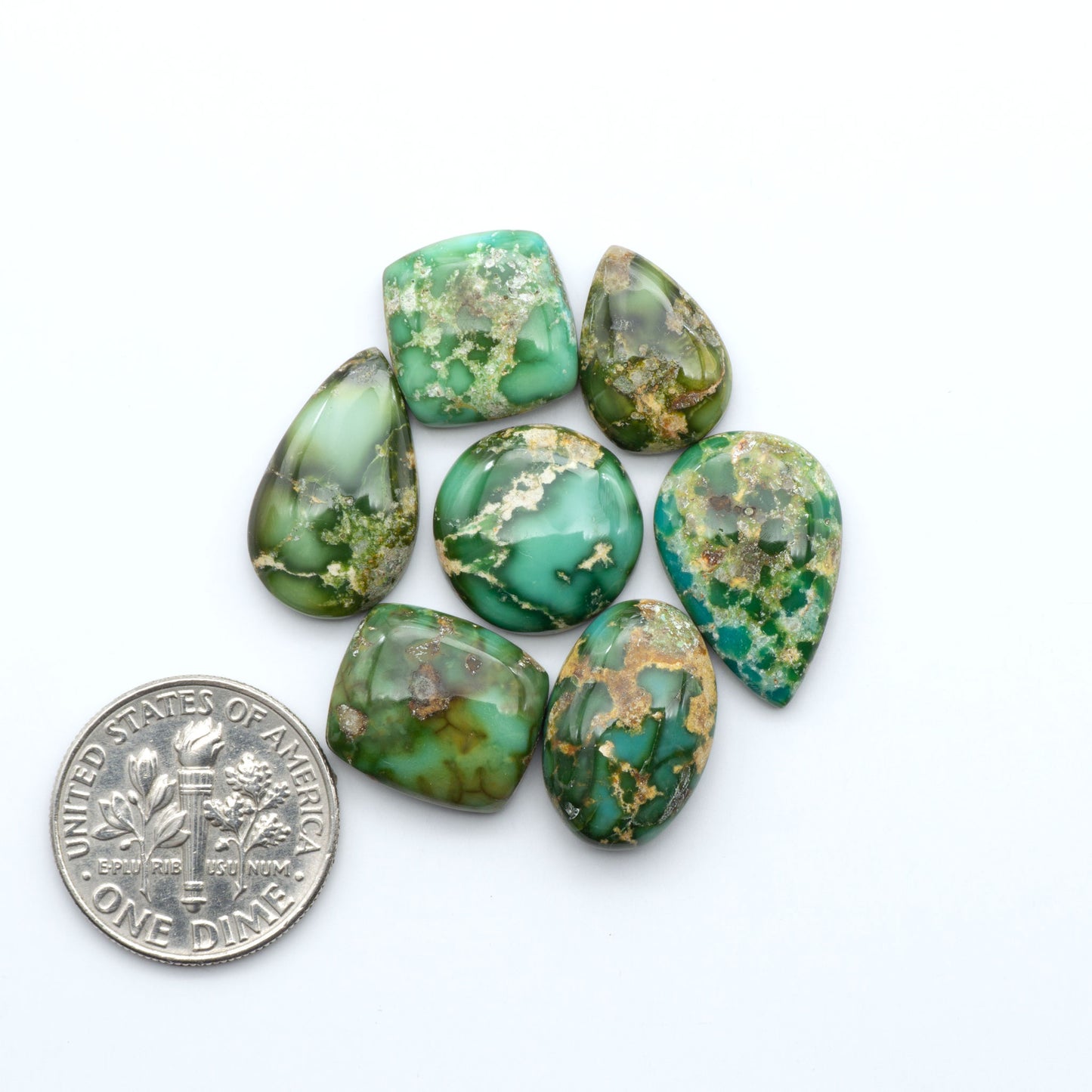 Sonoran Mountain Turquoise cabochons, blue-green color with natural matrix, polished stones on a white background, with a US dime for scale
