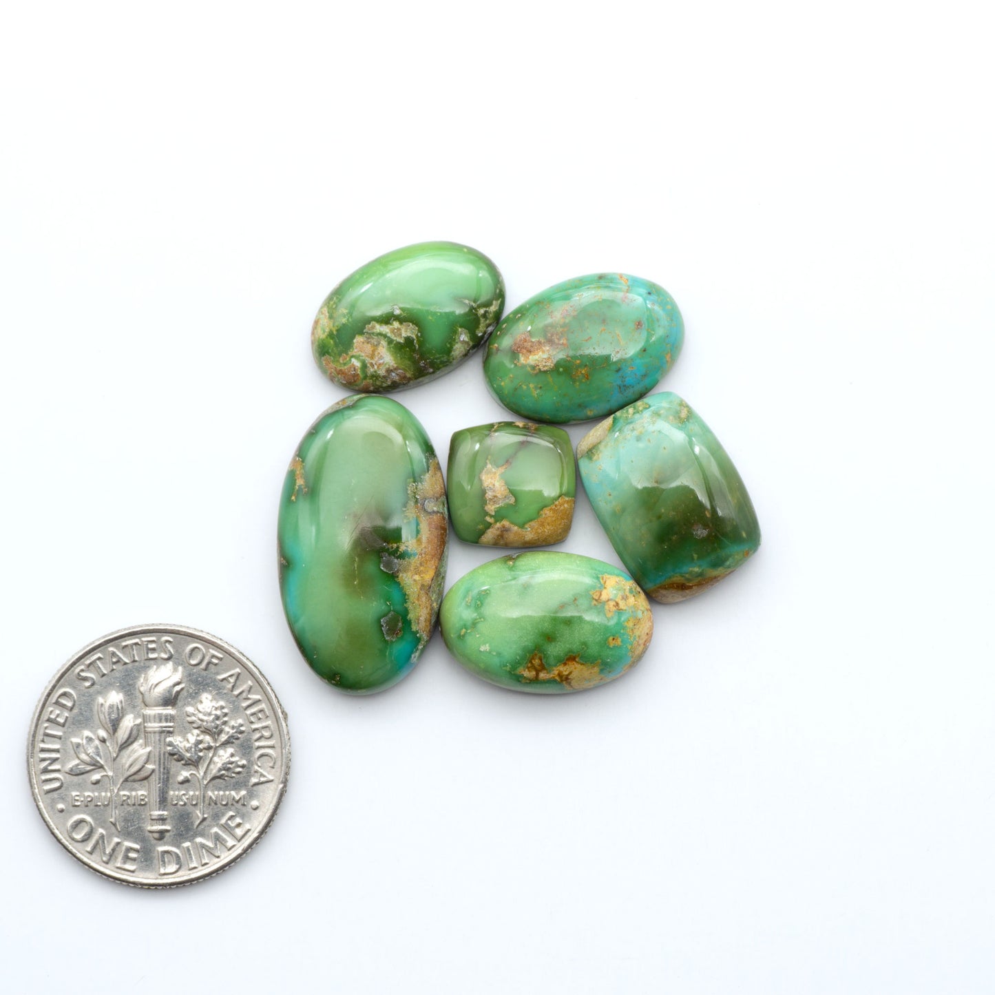 Sonoran Mountain Turquoise cabochons, blue-green color with natural matrix, polished stones on a white background, with a US dime for scale