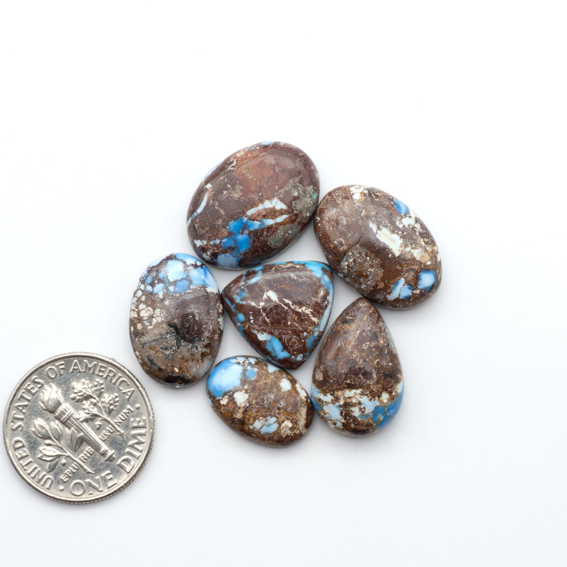 Golden Hills Turquoise cabochons, icy blue to lavender tones with chocolate matrix, polished stones on a white background with a US dime for scale