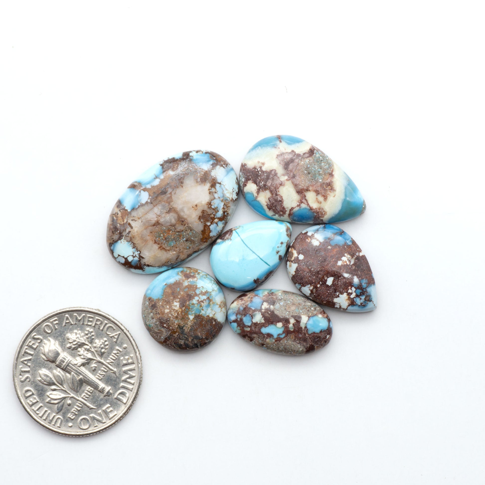 Golden Hills Turquoise cabochons, icy blue to lavender tones with chocolate matrix, polished stones on a white background with a US dime for scale