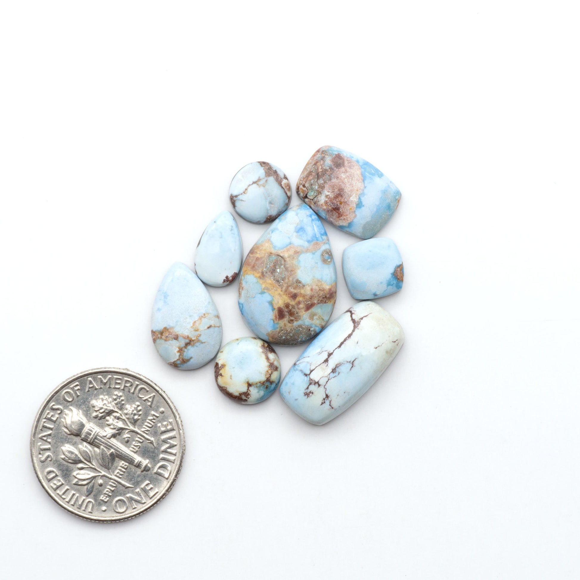 Golden Hills Turquoise cabochons, icy blue to lavender tones with chocolate matrix, polished stones on a white background with a US dime for scale