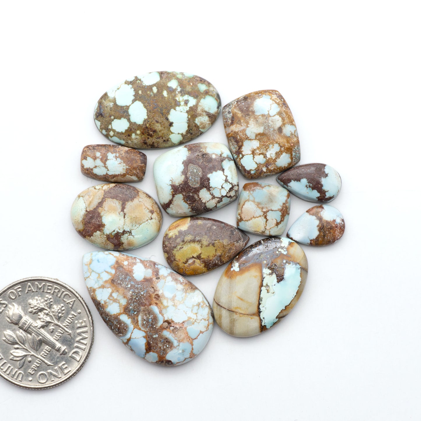 Golden Hills Turquoise cabochons, icy blue to lavender tones with chocolate matrix, polished stones on a white background with a US dime for scale