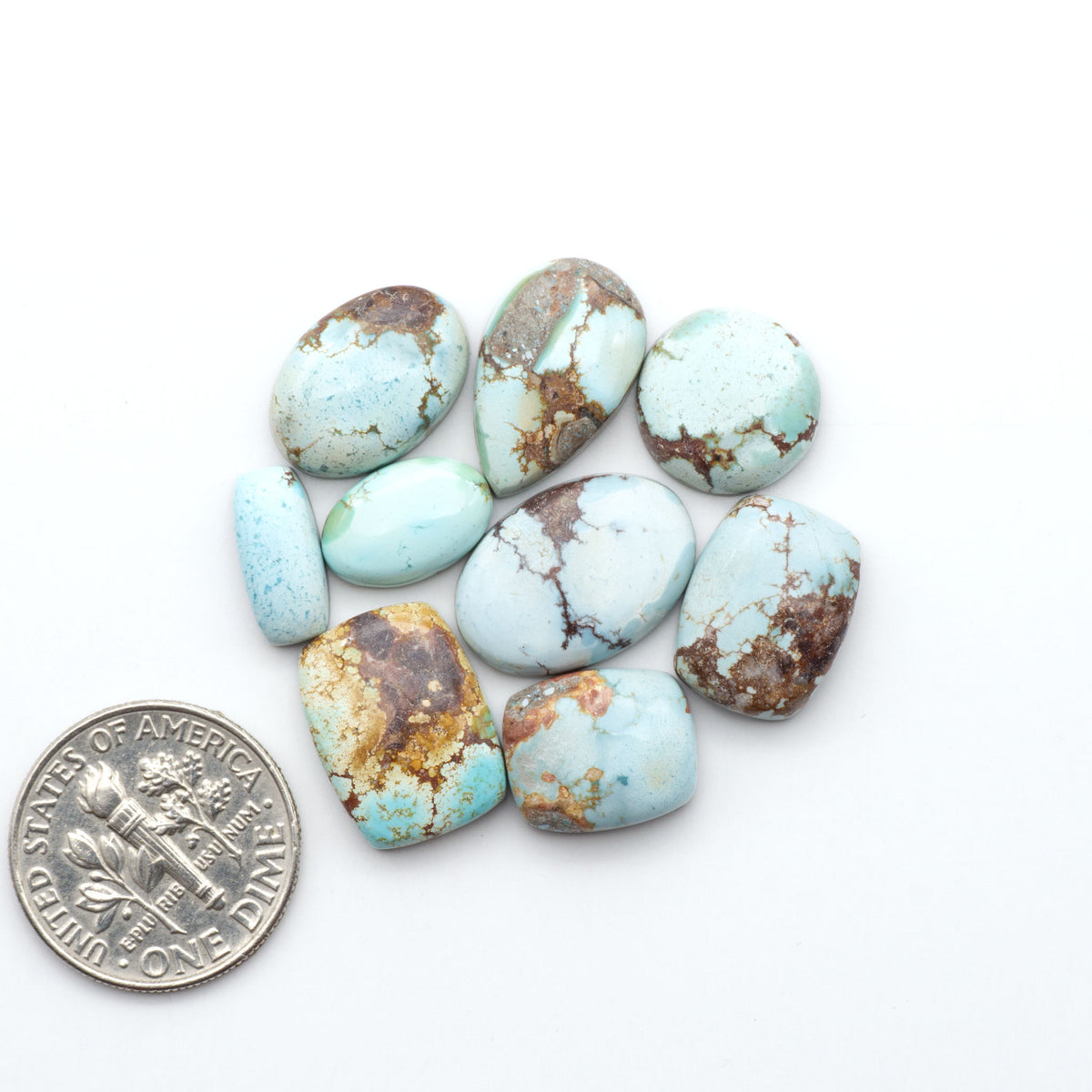 Golden Hills Turquoise cabochons, icy blue to lavender tones with chocolate matrix, polished stones on a white background with a US dime for scale