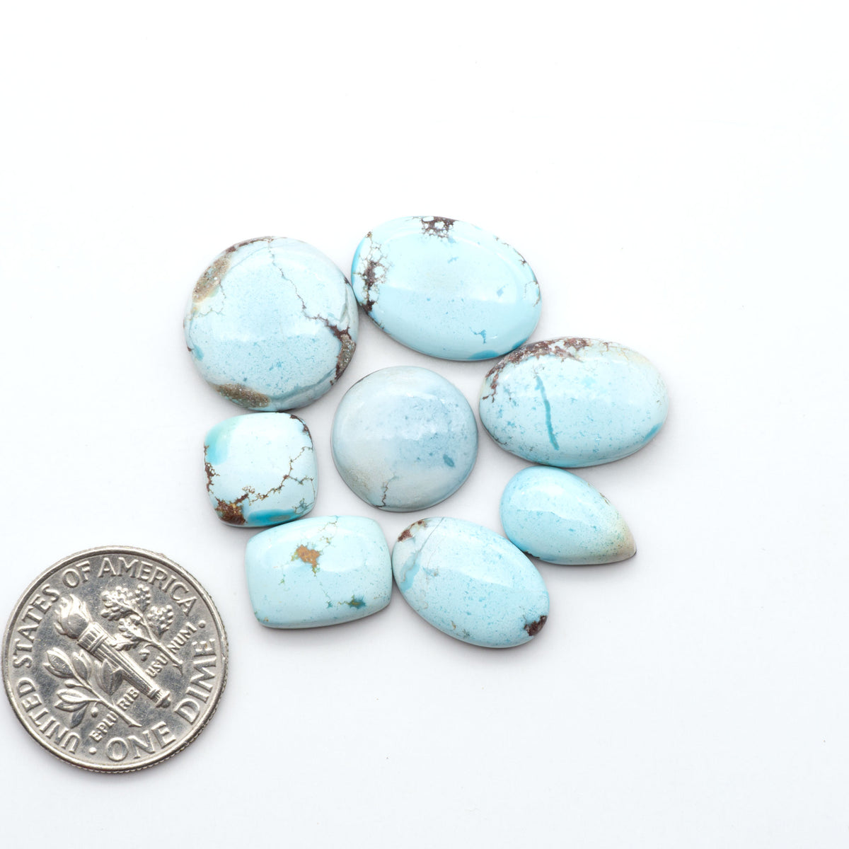 Golden Hills Turquoise cabochons, icy blue to lavender tones with chocolate matrix, polished stones on a white background with a US dime for scale