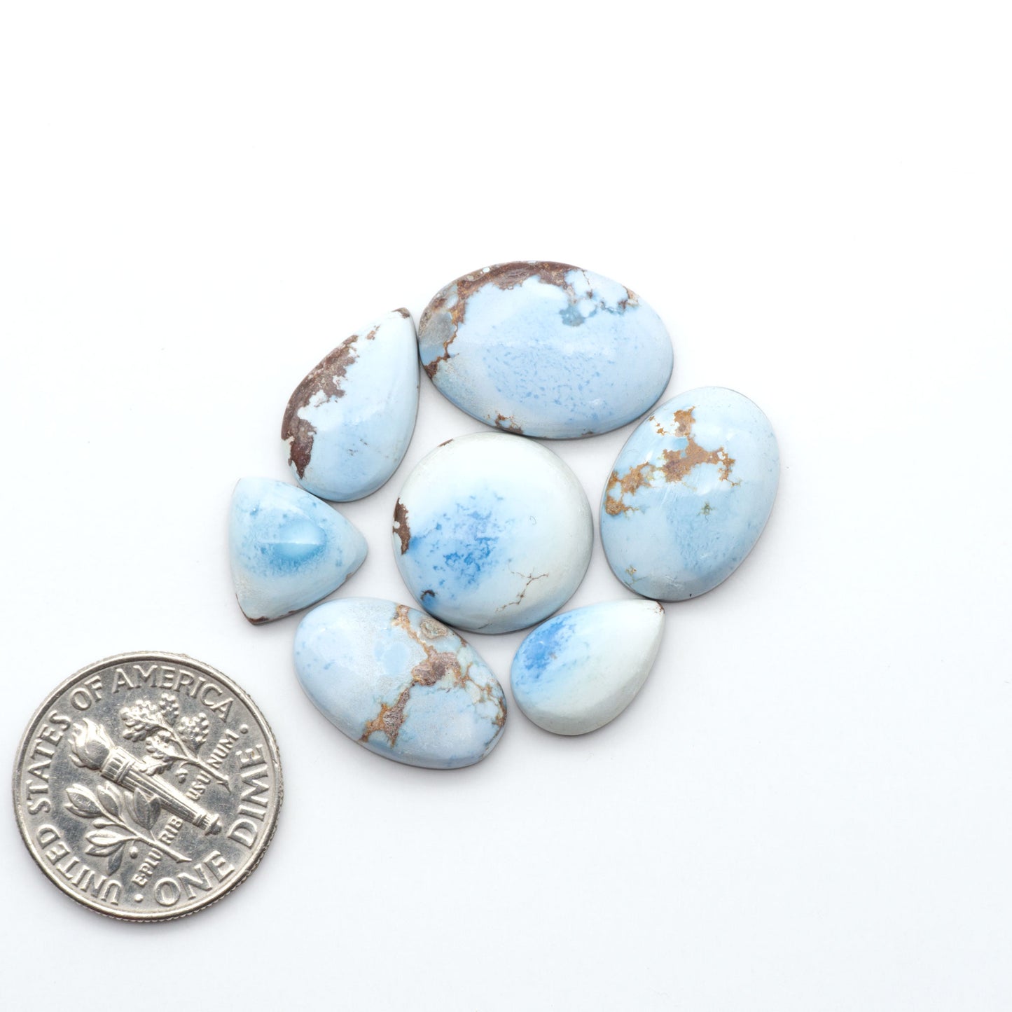 Golden Hills Turquoise cabochons, icy blue to lavender tones with chocolate matrix, polished stones on a white background with a US dime for scale