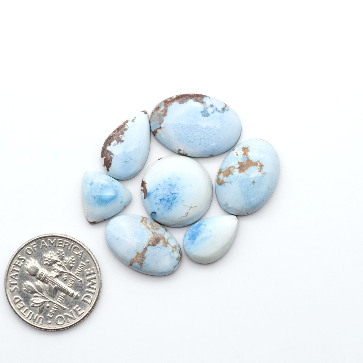 Golden Hills Turquoise cabochons, icy blue to lavender tones with chocolate matrix, polished stones on a white background with a US dime for scale