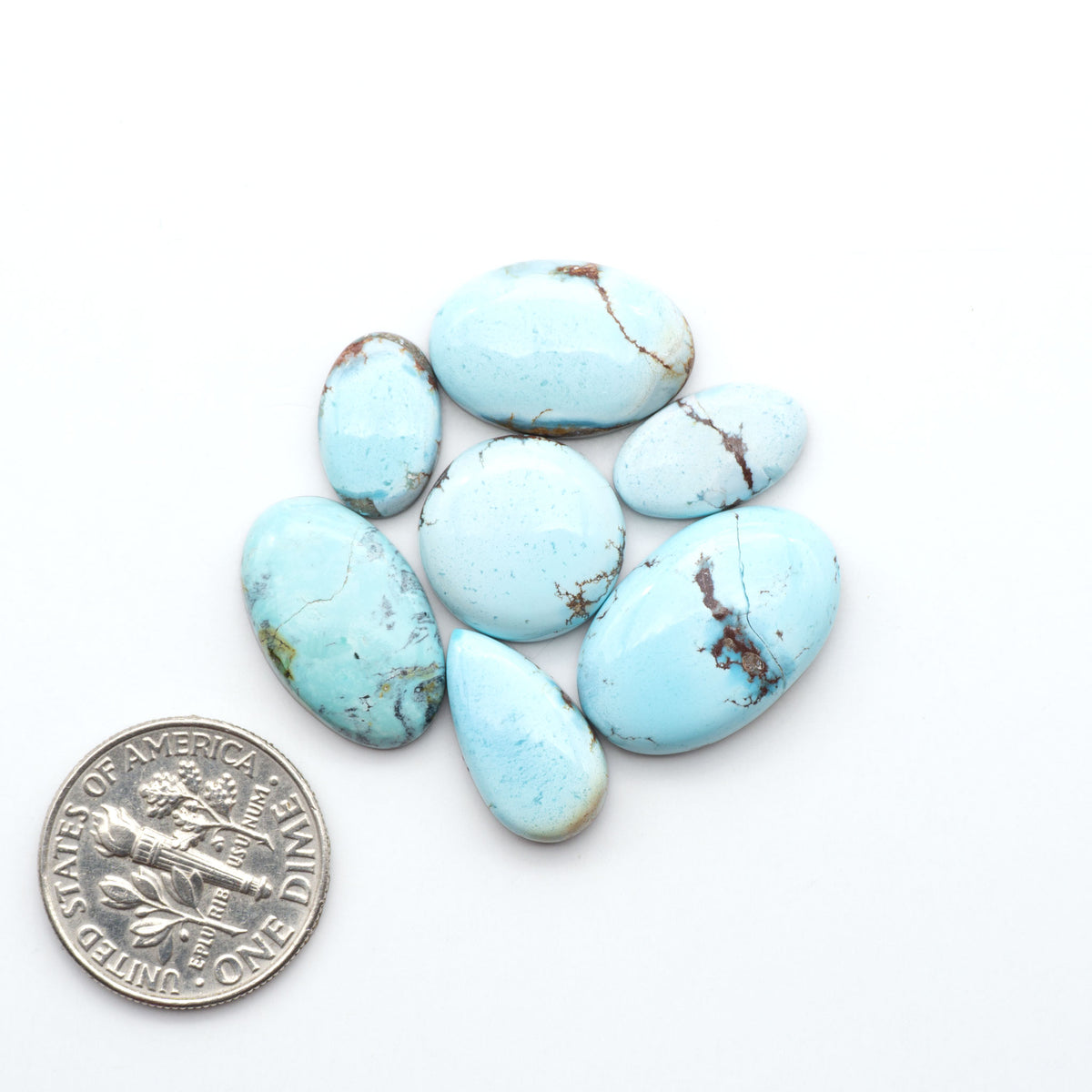 Golden Hills Turquoise cabochons, icy blue to lavender tones with chocolate matrix, polished stones on a white background with a US dime for scale