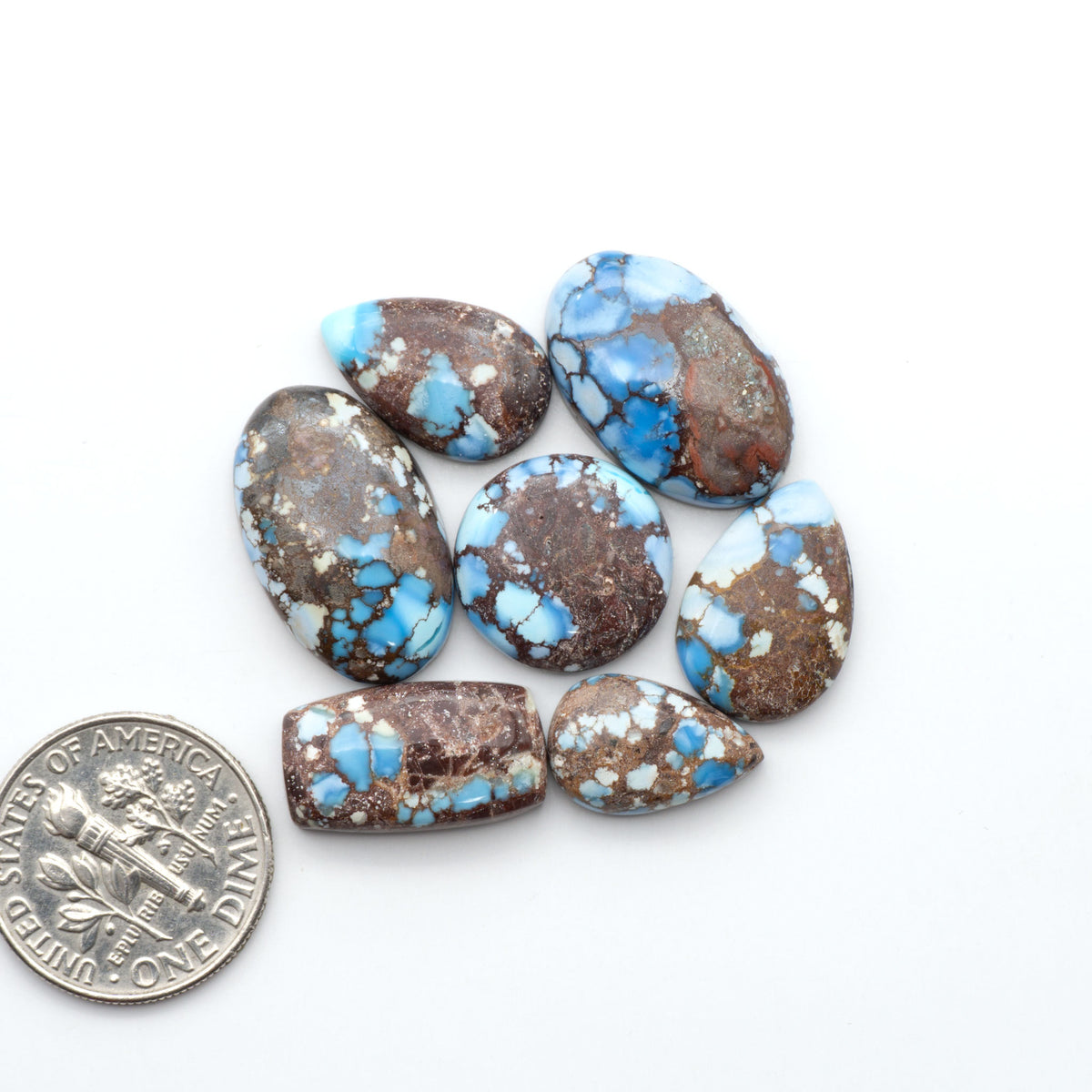 Golden Hills Turquoise cabochons, icy blue to lavender tones with chocolate matrix, polished stones on a white background with a US dime for scale