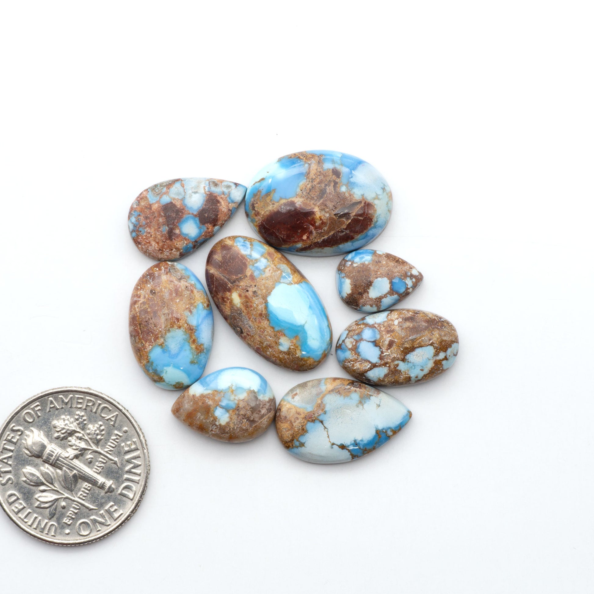 Golden Hills Turquoise cabochons, icy blue to lavender tones with chocolate matrix, polished stones on a white background with a US dime for scale