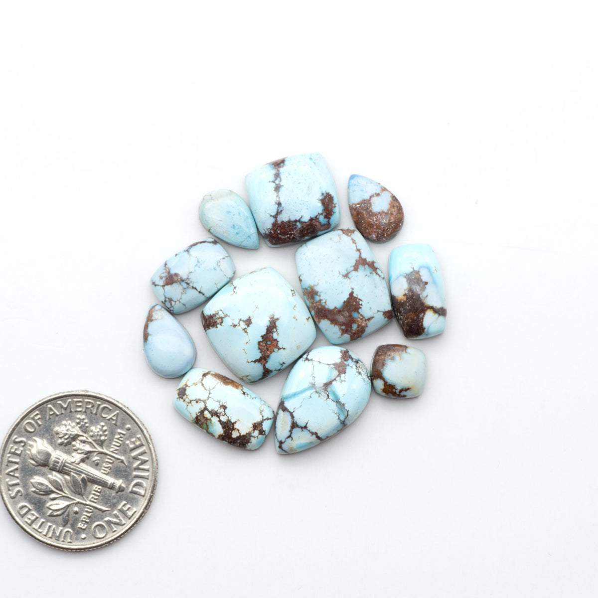 Golden Hills Turquoise cabochons, icy blue to lavender tones with chocolate matrix, polished stones on a white background with a US dime for scale