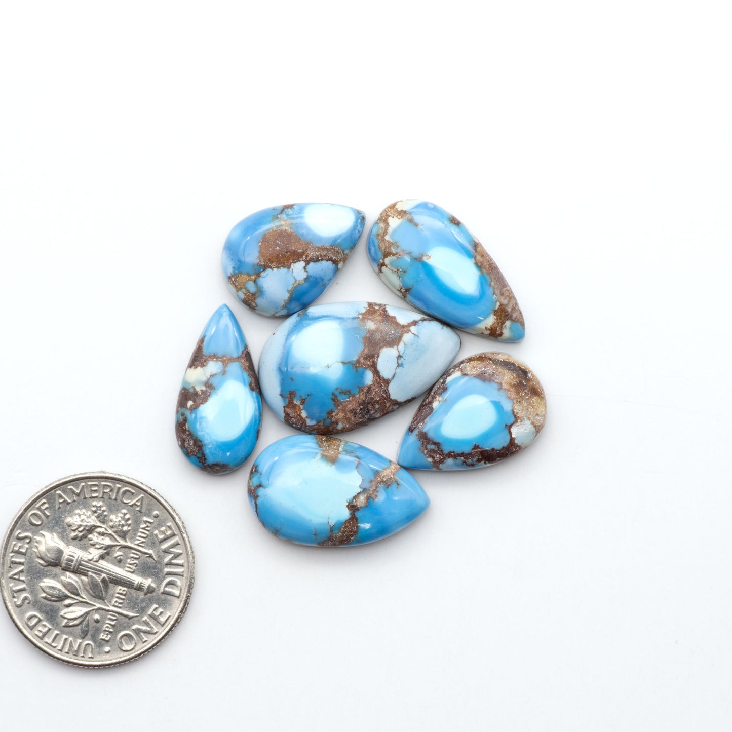 Golden Hills Turquoise cabochons, icy blue to lavender tones with chocolate matrix, polished stones on a white background with a US dime for scale