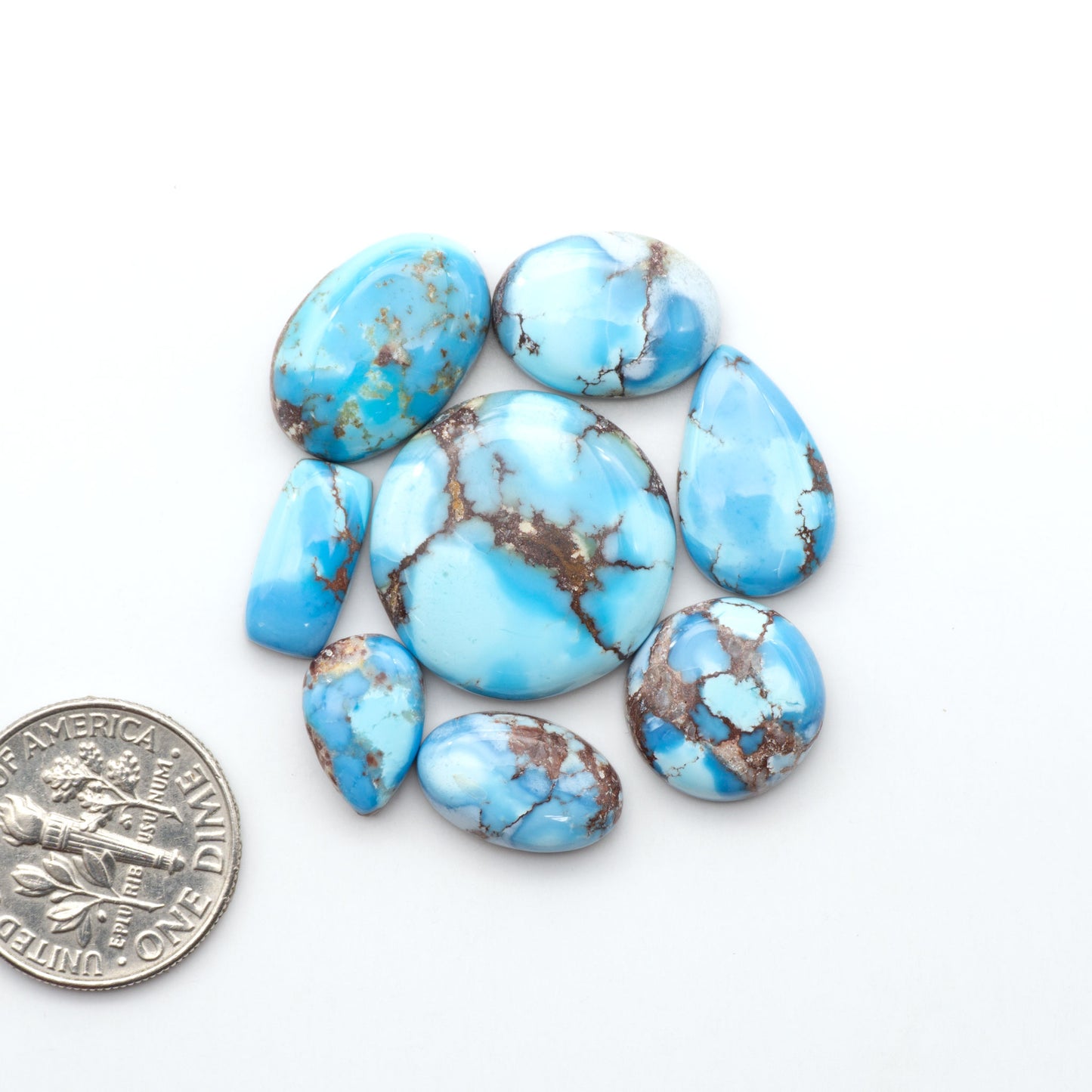 Golden Hills Turquoise cabochons, icy blue to lavender tones with chocolate matrix, polished stones on a white background with a US dime for scale