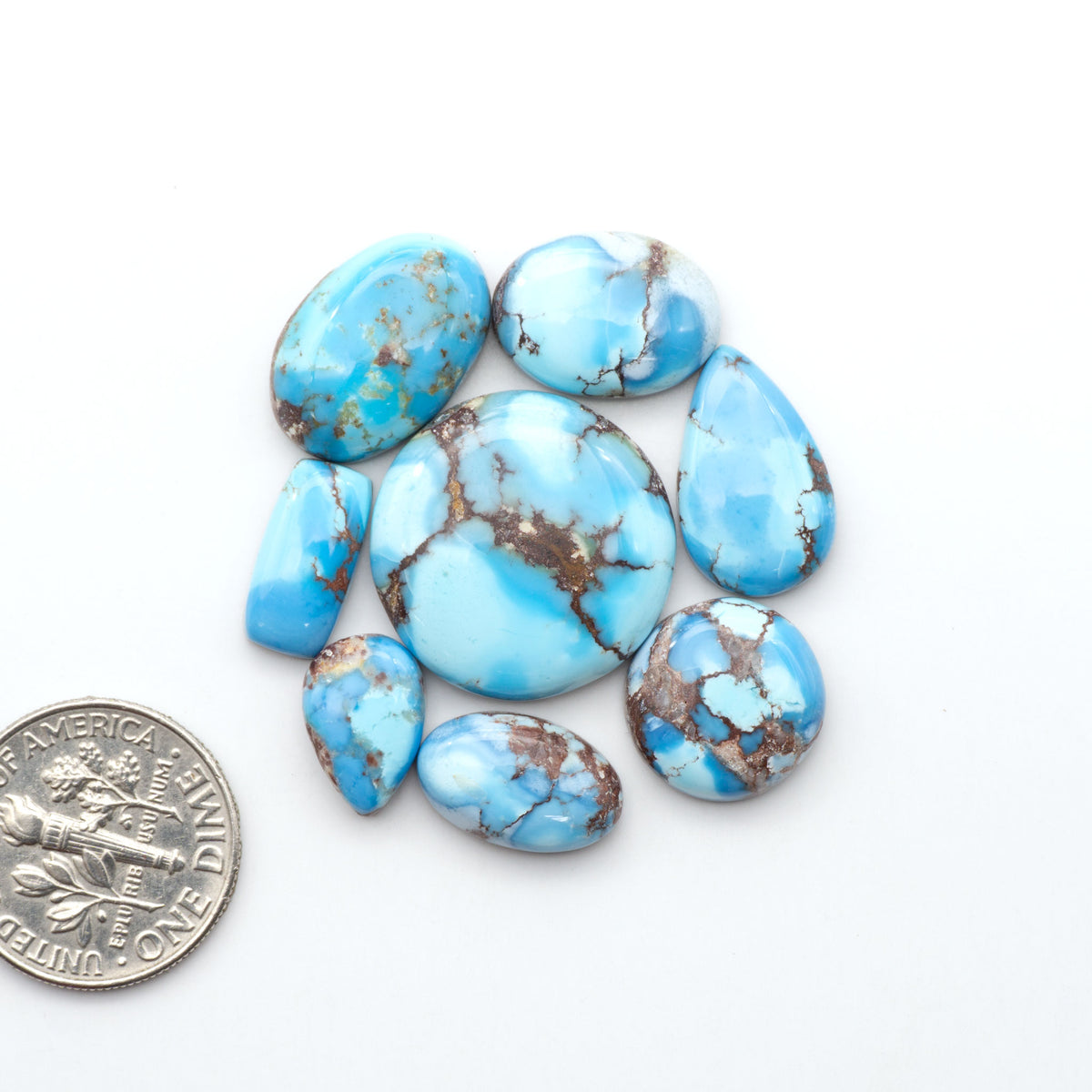 Golden Hills Turquoise cabochons, icy blue to lavender tones with chocolate matrix, polished stones on a white background with a US dime for scale