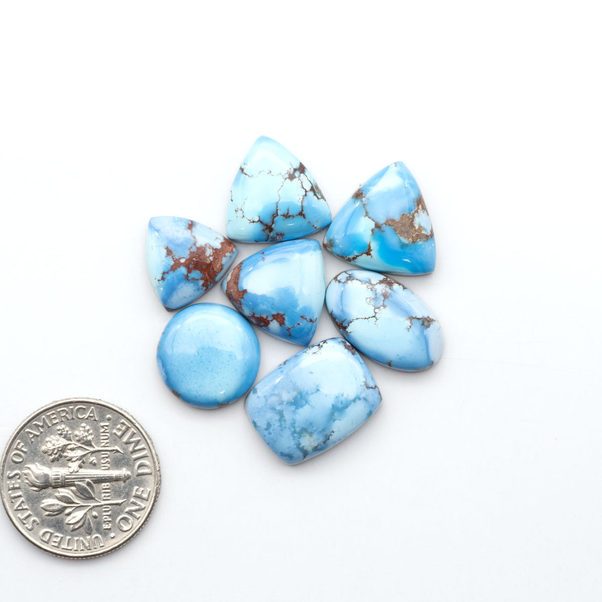 Golden Hills Turquoise cabochons, icy blue to lavender tones with chocolate matrix, polished stones on a white background with a US dime for scale