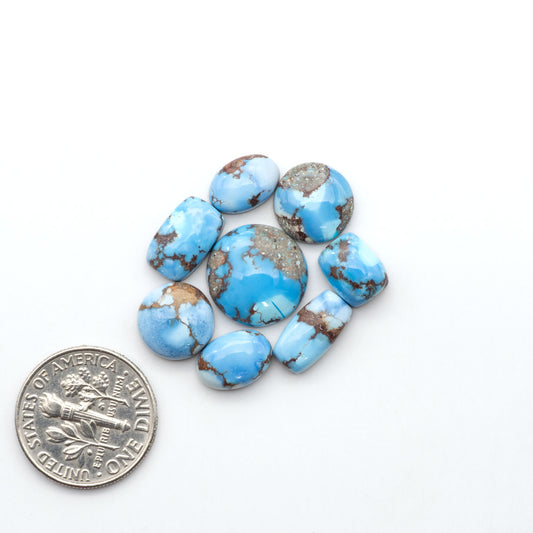 Golden Hills Turquoise cabochons, icy blue to lavender tones with chocolate matrix, polished stones on a white background with a US dime for scale