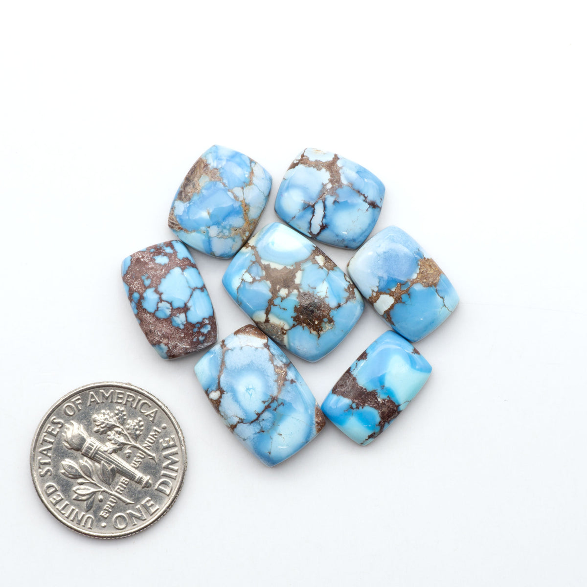 Golden Hills Turquoise cabochons, icy blue to lavender tones with chocolate matrix, polished stones on a white background with a US dime for scale