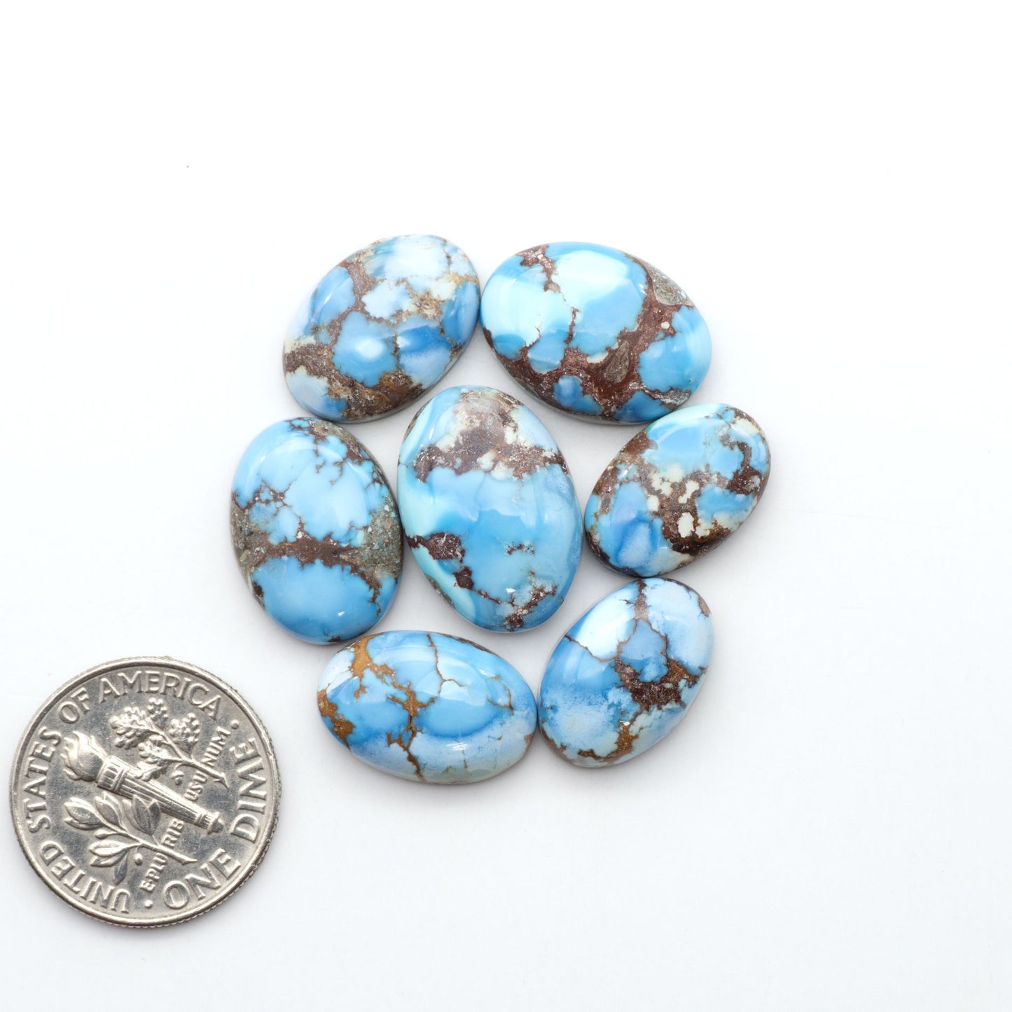 Golden Hills Turquoise cabochons, icy blue to lavender tones with chocolate matrix, polished stones on a white background with a US dime for scale