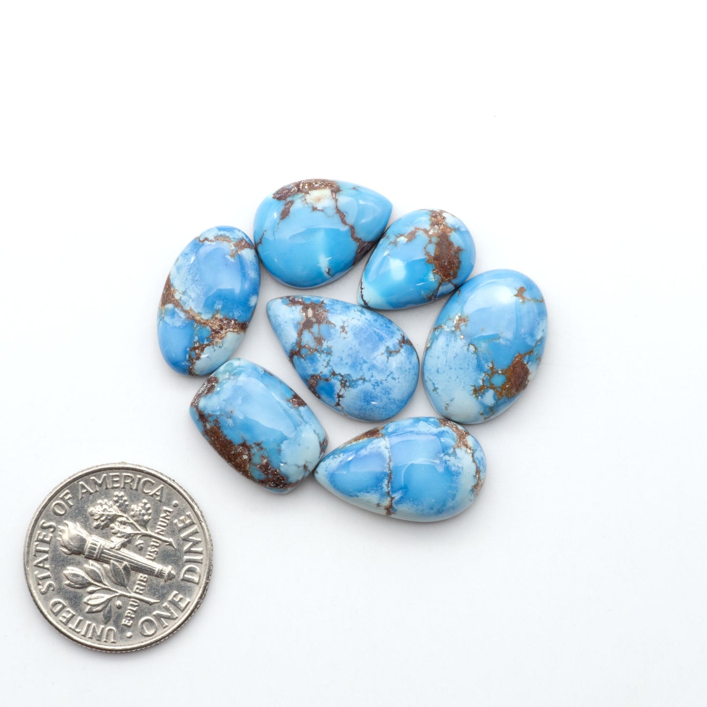 Golden Hills Turquoise cabochons, icy blue to lavender tones with chocolate matrix, polished stones on a white background with a US dime for scale