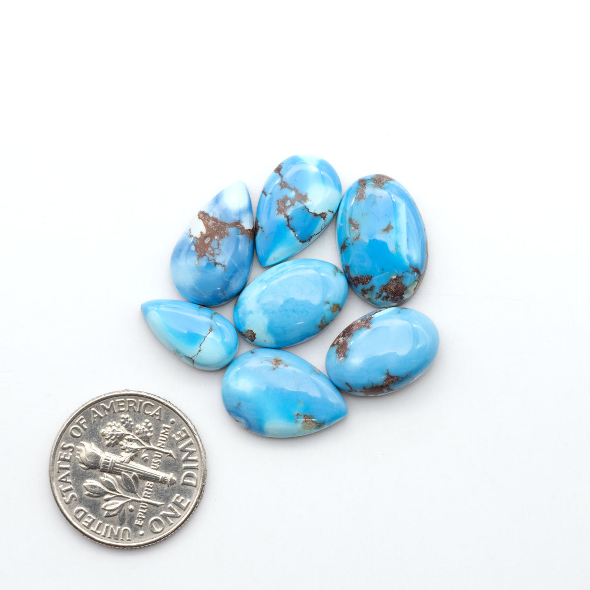 Golden Hills Turquoise cabochons, icy blue to lavender tones with chocolate matrix, polished stones on a white background with a US dime for scale
