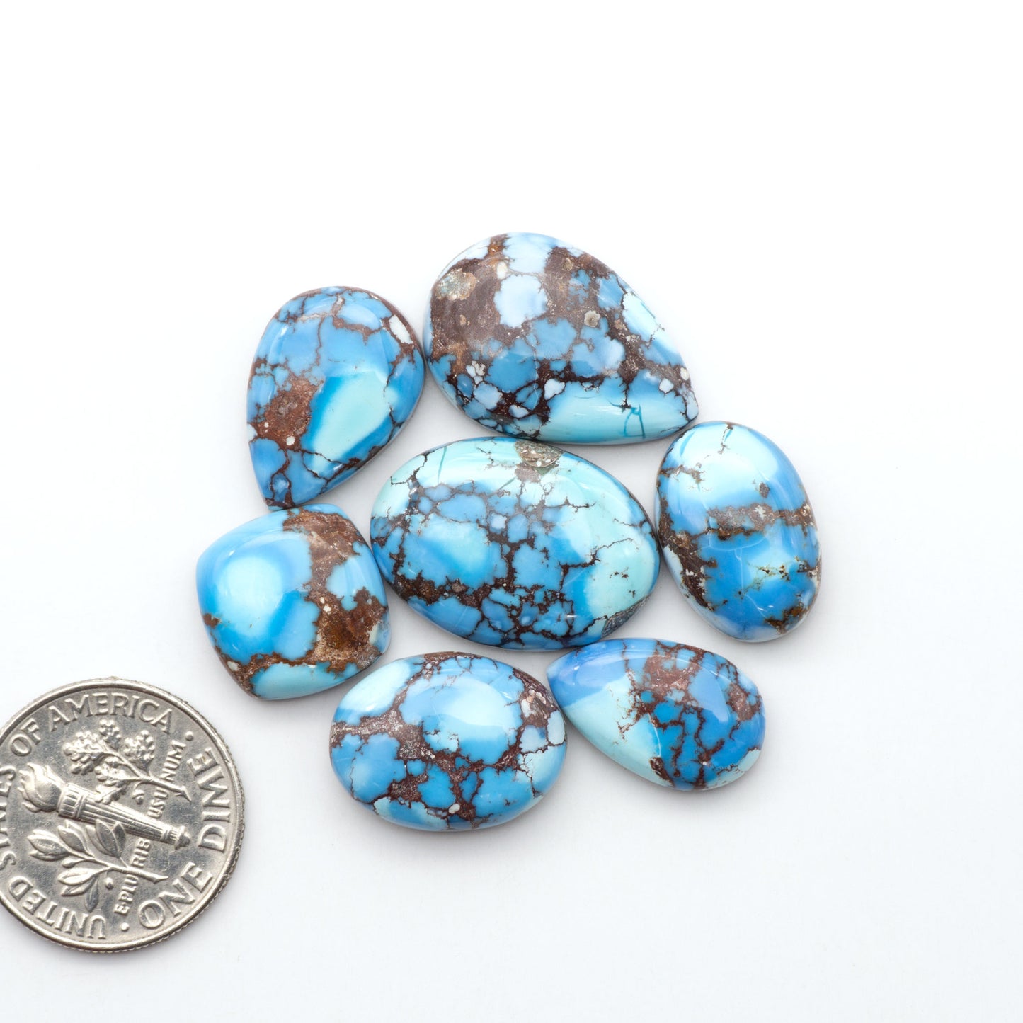 Golden Hills Turquoise cabochons, icy blue to lavender tones with chocolate matrix, polished stones on a white background with a US dime for scale