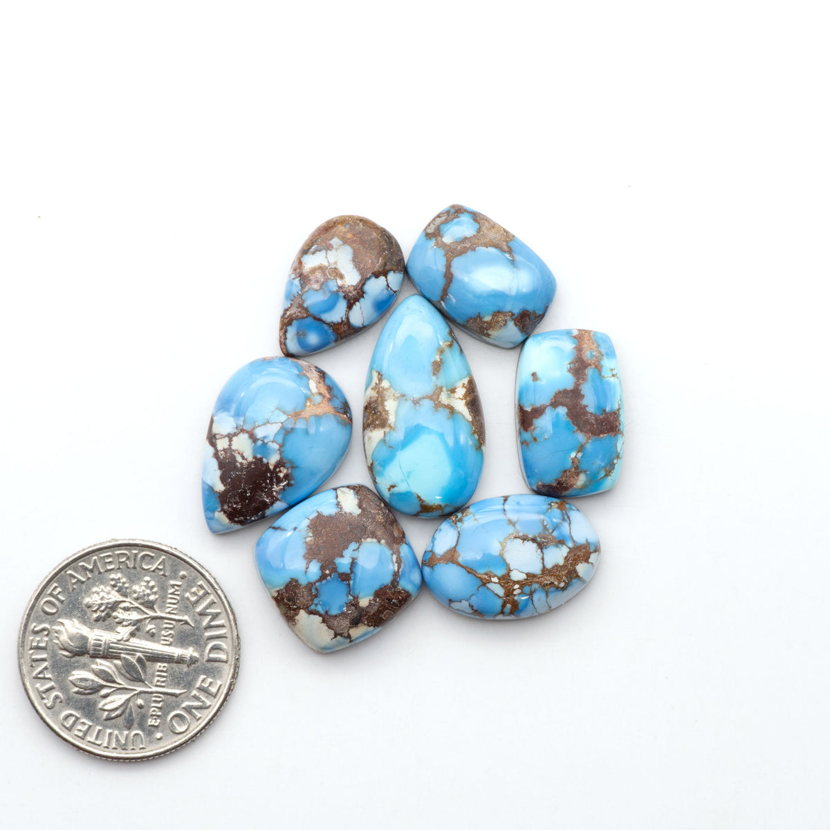 Golden Hills Turquoise cabochons, icy blue to lavender tones with chocolate matrix, polished stones on a white background with a US dime for scale