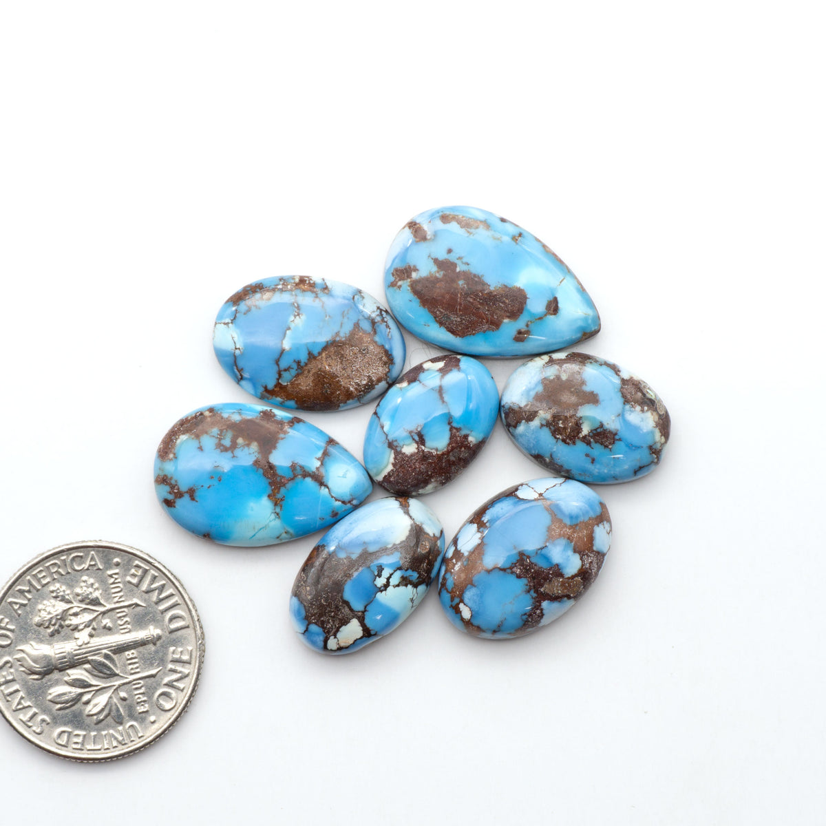 Golden Hills Turquoise cabochons, icy blue to lavender tones with chocolate matrix, polished stones on a white background with a US dime for scale