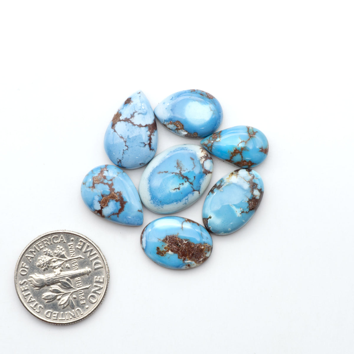 Golden Hills Turquoise cabochons, icy blue to lavender tones with chocolate matrix, polished stones on a white background with a US dime for scale