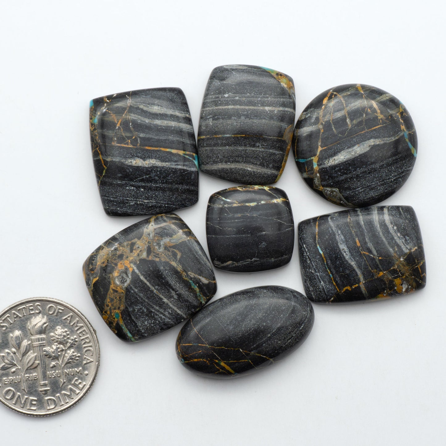 Black Jack turquoise cabochons, blue-green color with black matrix, polished stones on a white background with a US dime for scale
