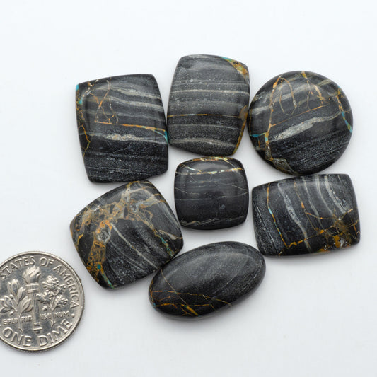Black Jack turquoise cabochons, blue-green color with black matrix, polished stones on a white background with a US dime for scale