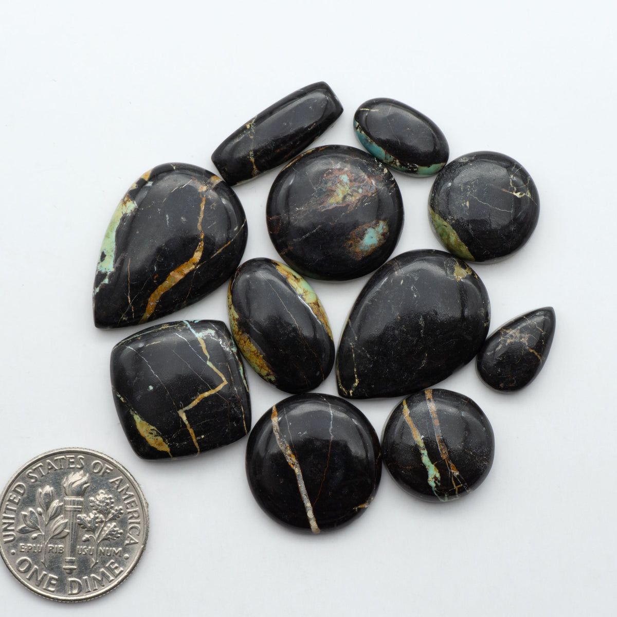 Black Jack turquoise cabochons, blue-green color with black matrix, polished stones on a white background with a US dime for scale