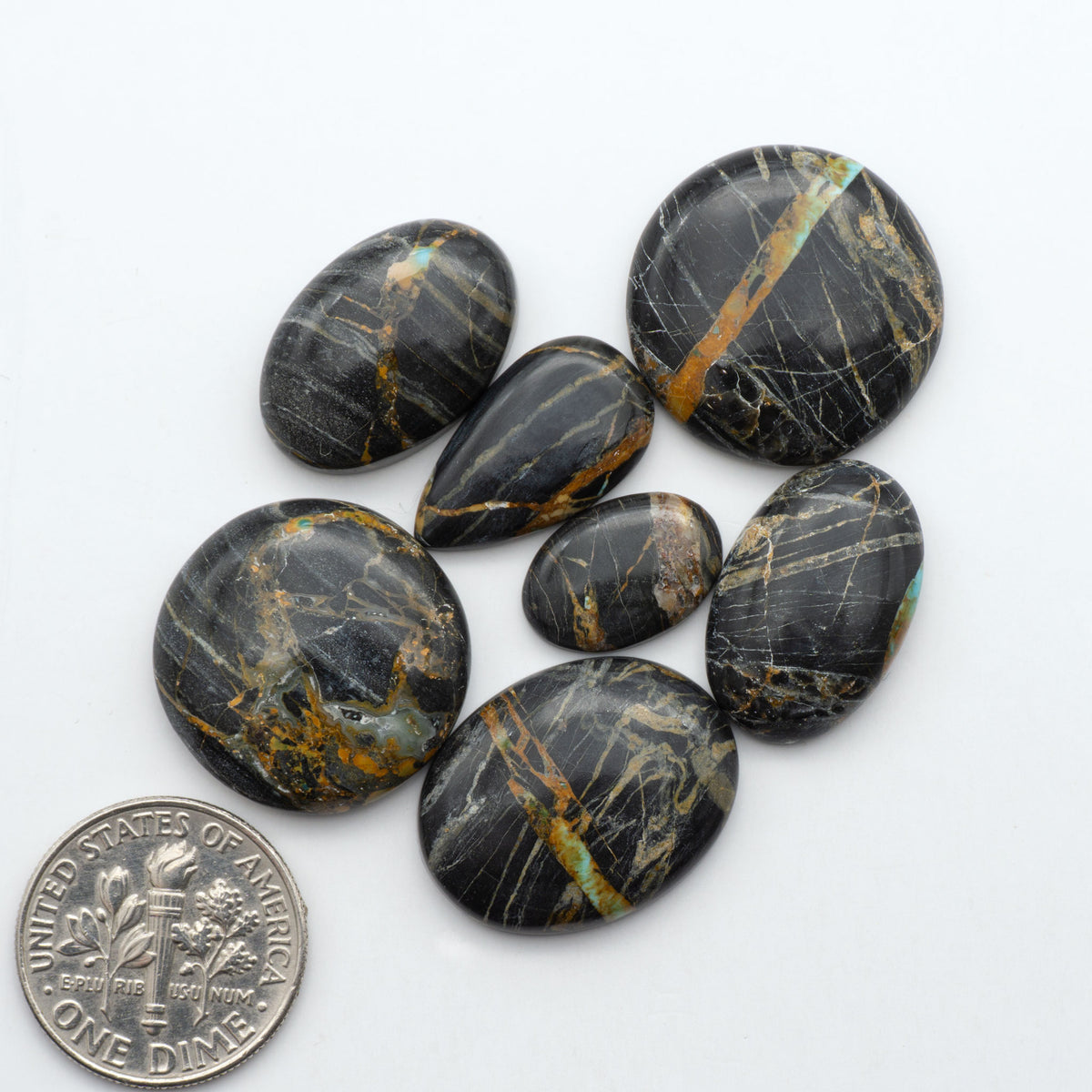 Black Jack turquoise cabochons, blue-green color with black matrix, polished stones on a white background with a US dime for scale