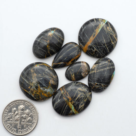 Black Jack turquoise cabochons, blue-green color with black matrix, polished stones on a white background with a US dime for scale